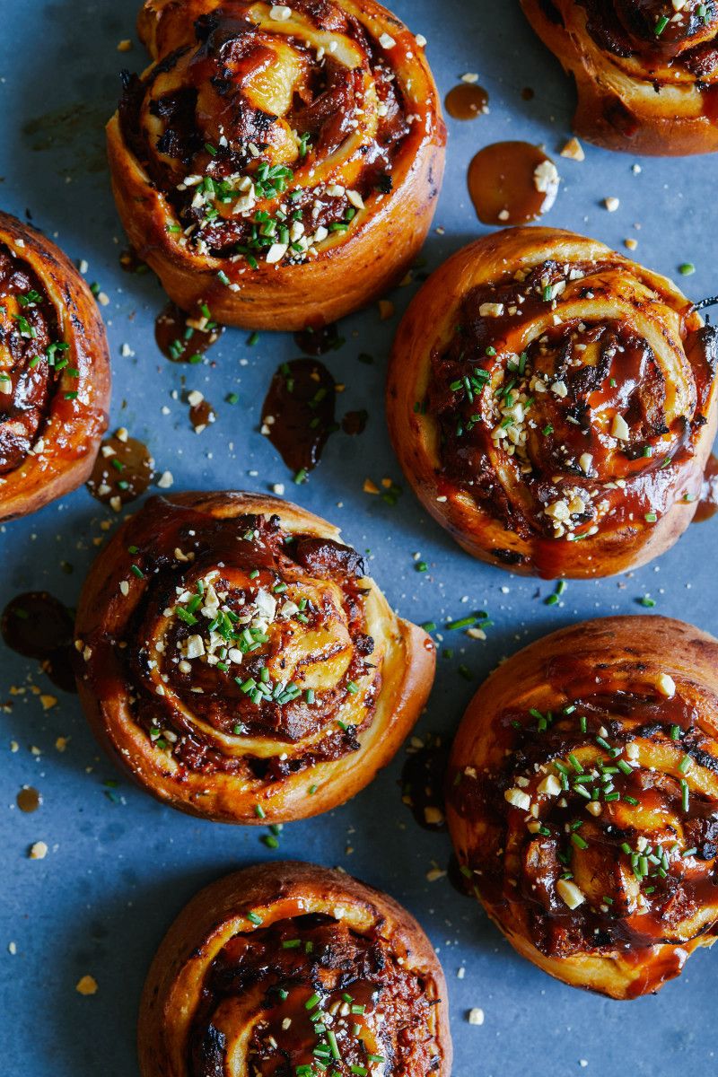 Close-up of several round, pulled pork-filled buns with glaze, chopped chives, and nuts on top