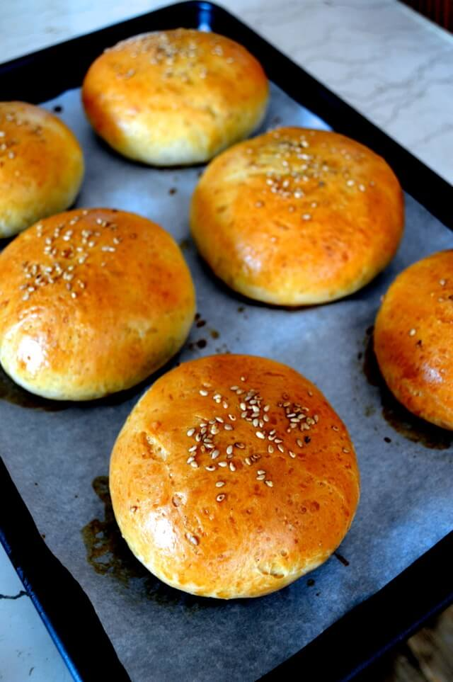 Baked, round, golden-brown buns with sesame seeds on top on a baking sheet lined with parchment paper.