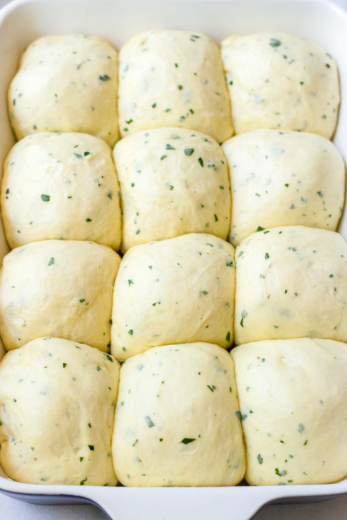 Unbaked garlic herb dinner rolls rising in a white baking dish