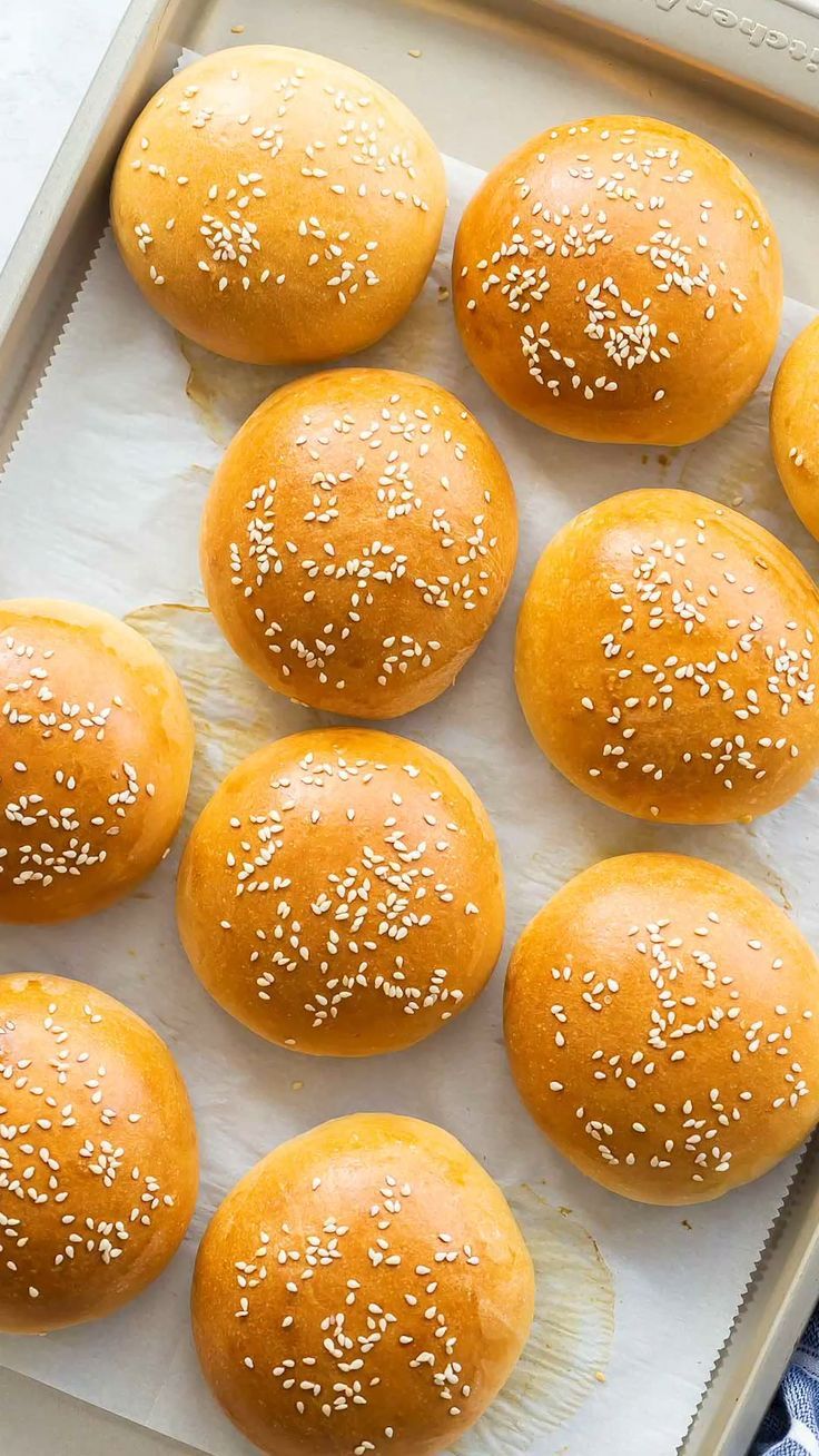 Round golden-brown sesame seed buns on a parchment-lined baking sheet.