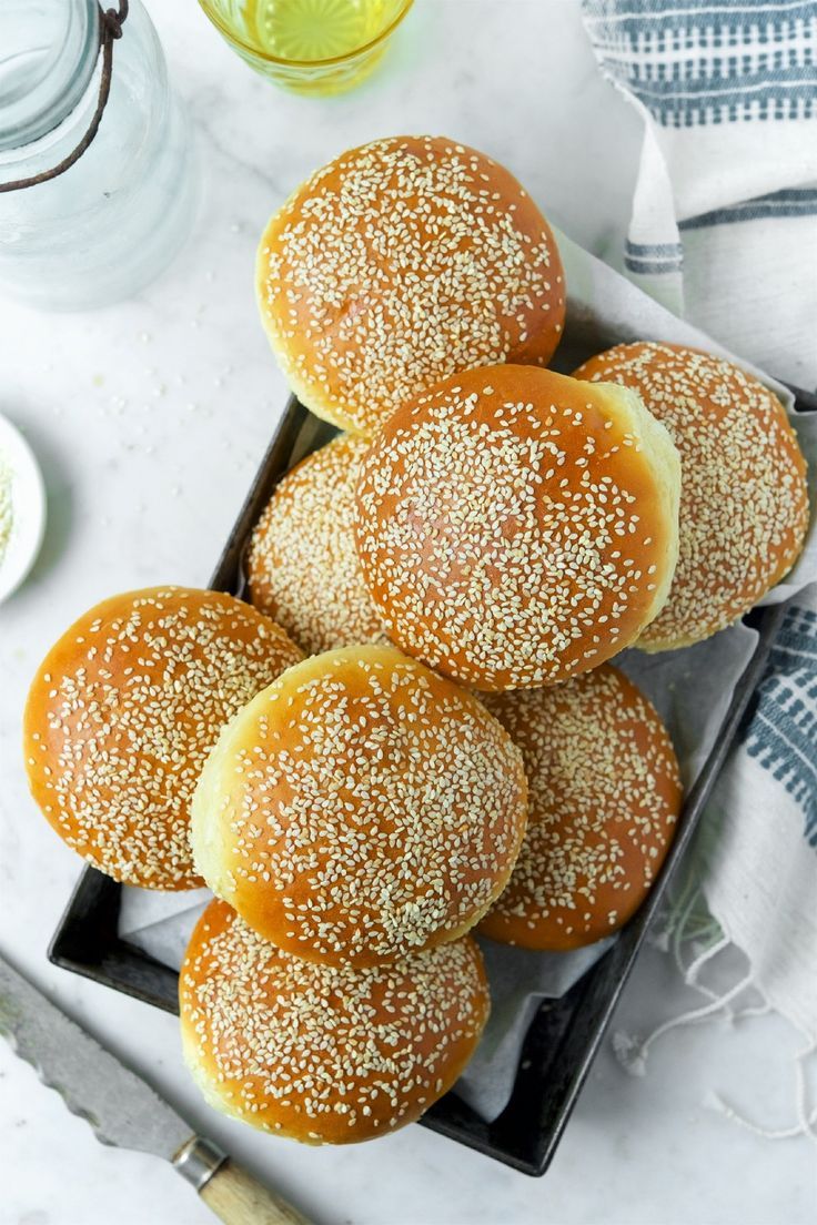 A metal tray holds several golden-brown burger buns, each topped with a generous sprinkle of sesame seeds.