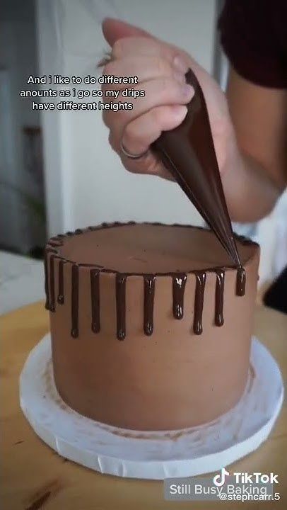 Hand piping chocolate ganache from a piping bag onto the top edge of a chocolate frosted cake to create drips.
