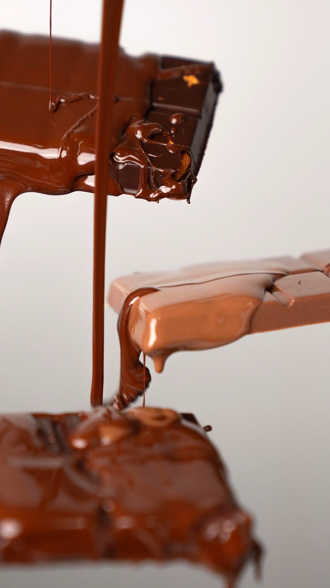 Melted dark and milk chocolate coating several chocolate bars as more chocolate drips down.