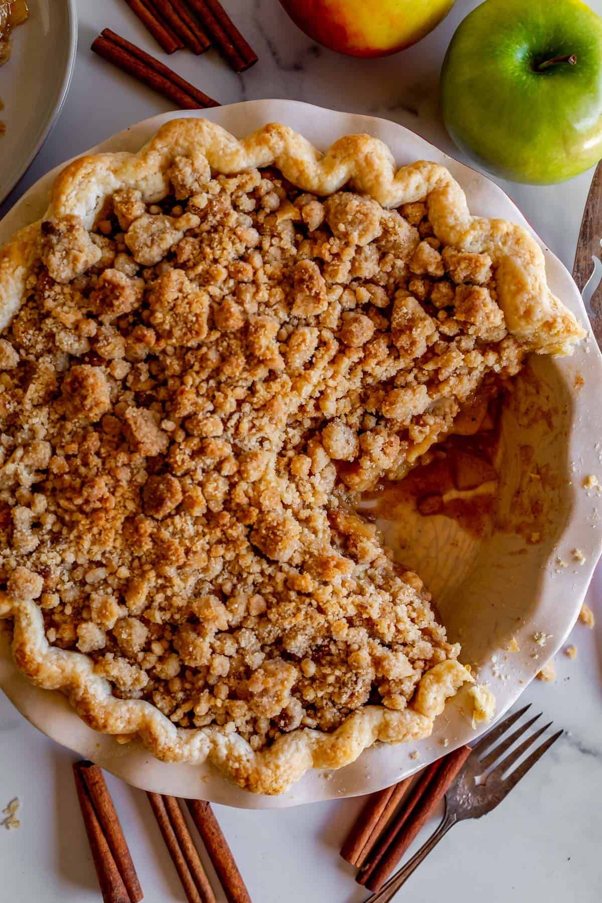 Baked Dutch apple pie with a generous crumb topping, served in a white pie dish with one slice removed