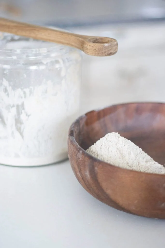 Bowl of flour beside a jar of sourdough starter