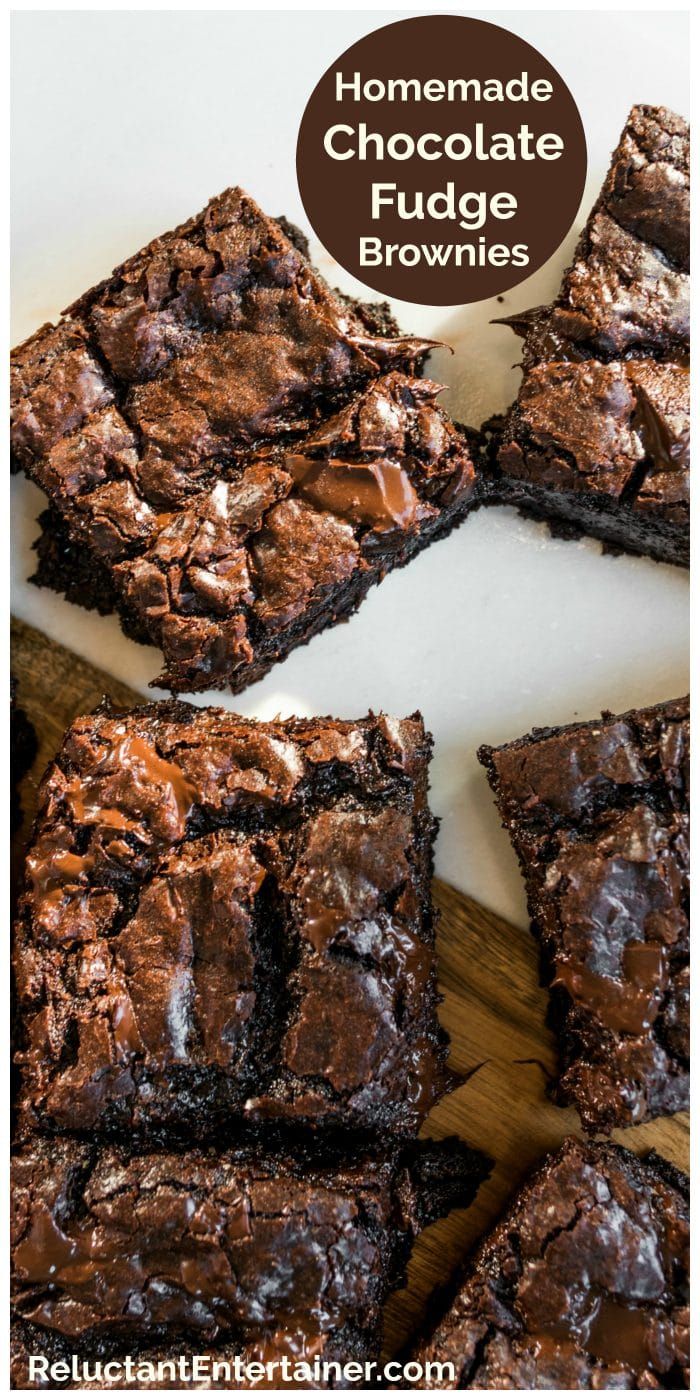 Several dark, rich chocolate fudge brownies with shiny tops, some with melted chocolate chips visible, arranged on a white…