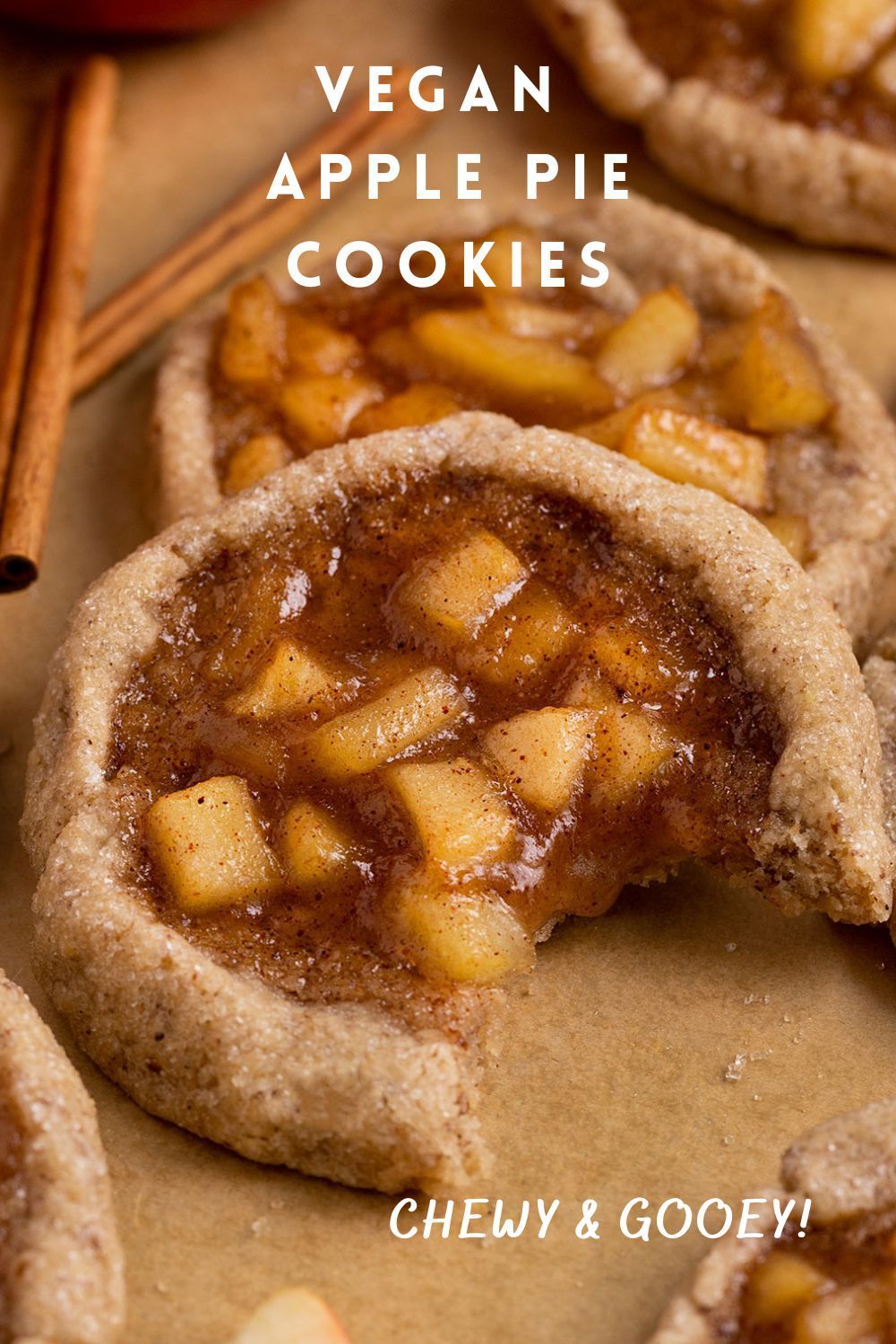 Close-up of a vegan apple pie cookie with a bite taken out, showing the chunky apple filling and a chewy crust.