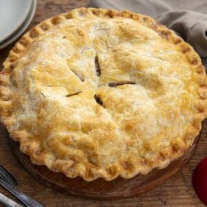 Golden brown baked apple pie with a crimped crust, resting on a wooden board.