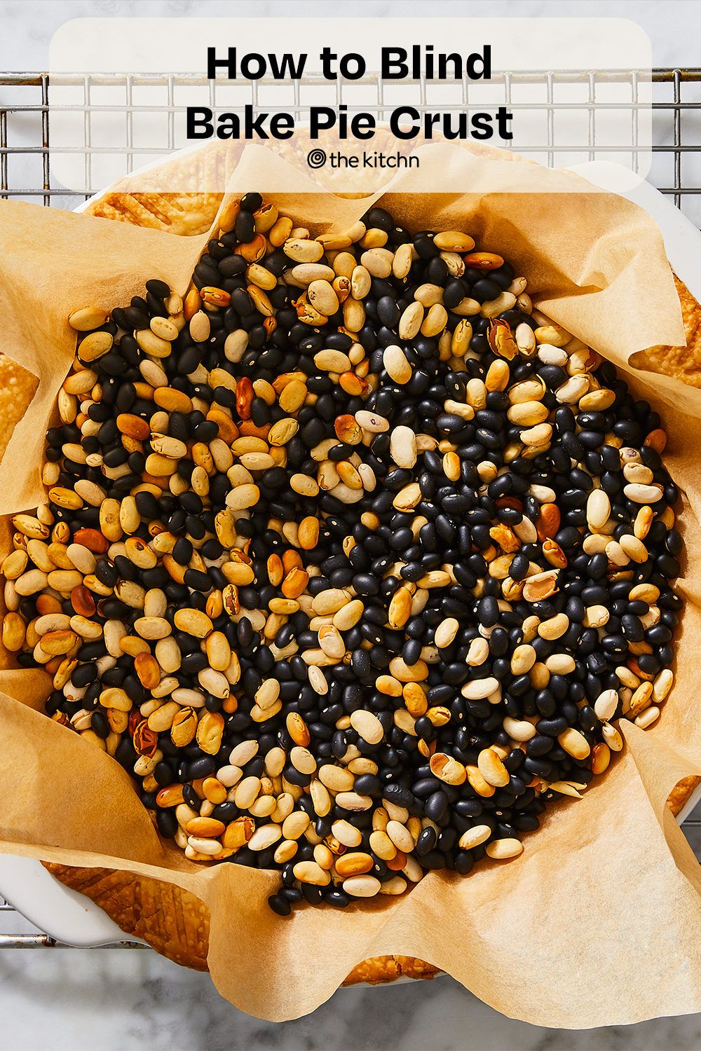 Close-up of a pie crust lined with parchment paper, filled with a mix of black and white dried beans.