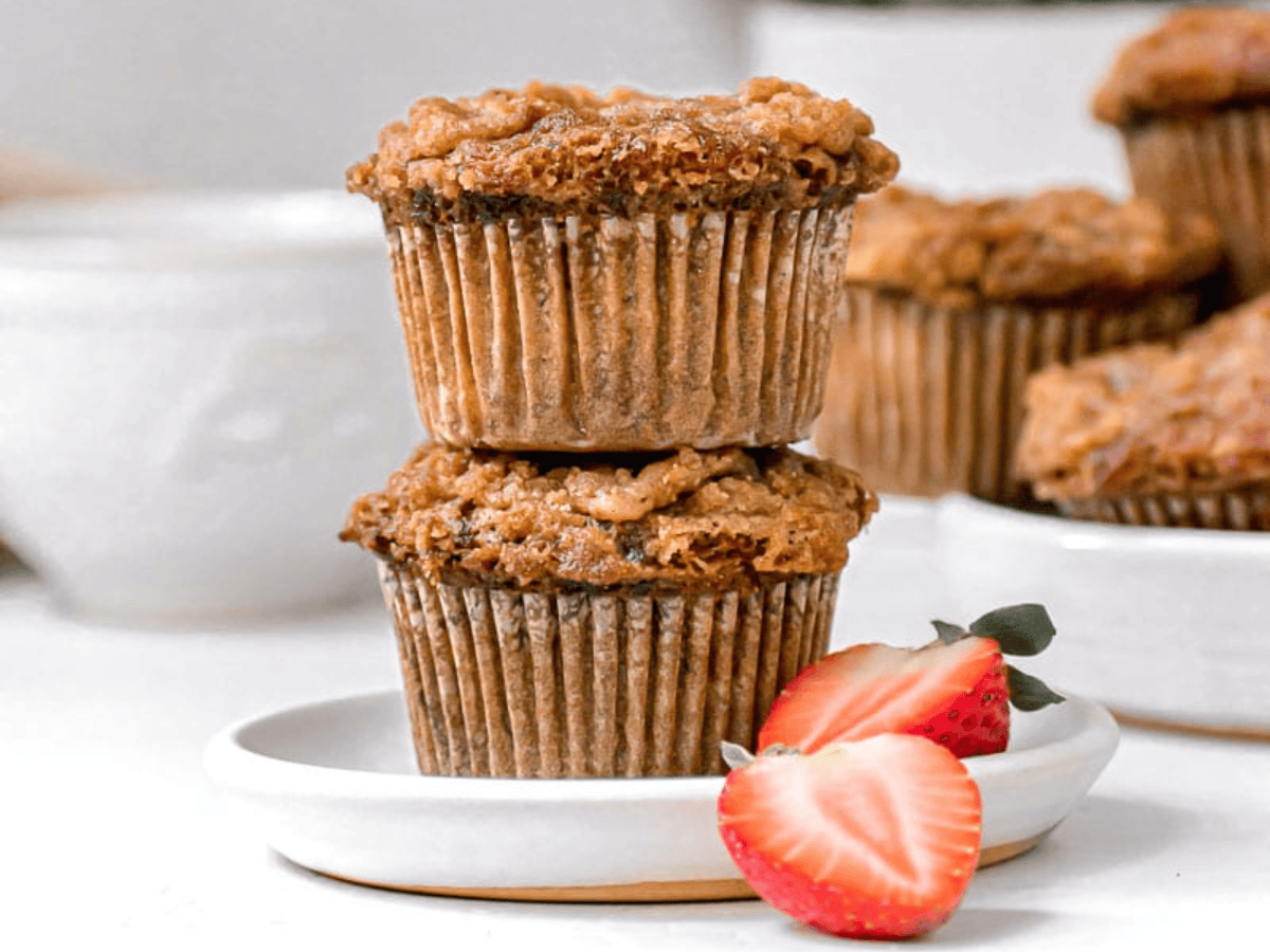Banana crumb muffins stacked on a white plate with a strawberry beside them