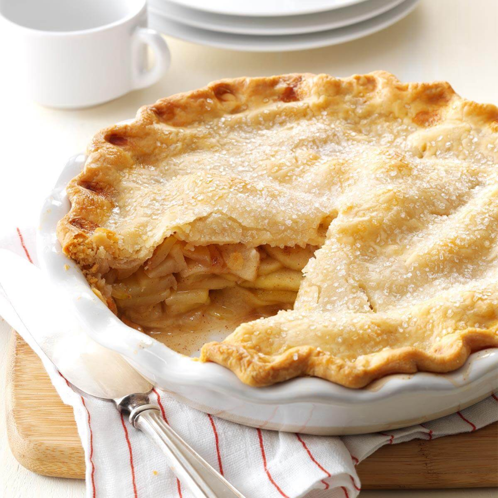 Baked apple pie in a white dish with one slice removed, showing the apple filling. A pie server is next to it.