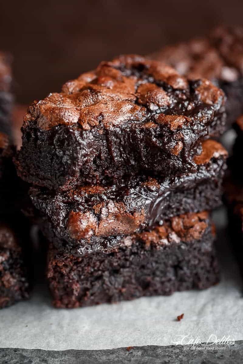 A stack of three rich, dark chocolate brownies with shiny, crinkly tops, exhibiting a dense, moist interior.