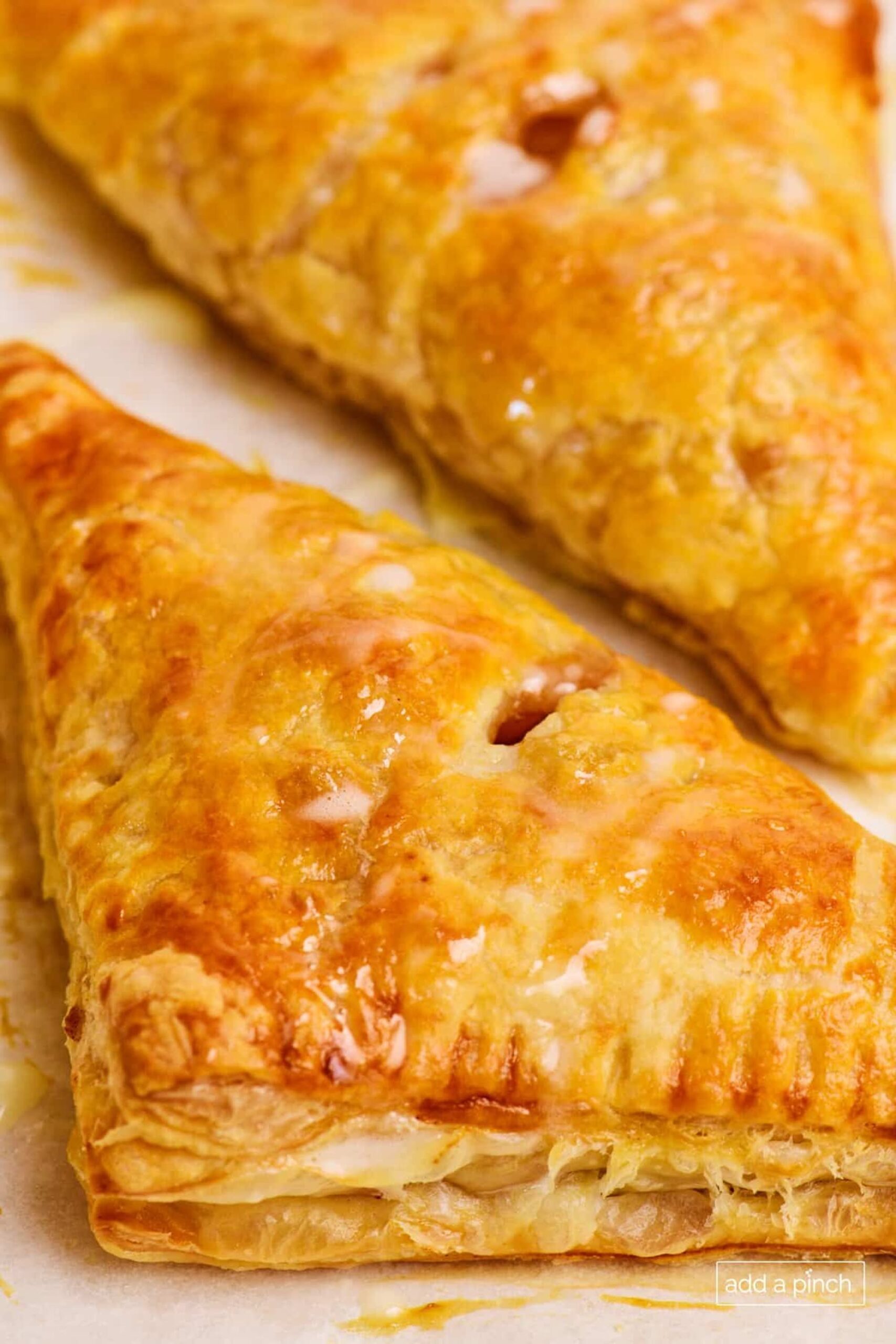 Close-up of a golden-baked apple turnover with a thin white glaze drizzled over the top