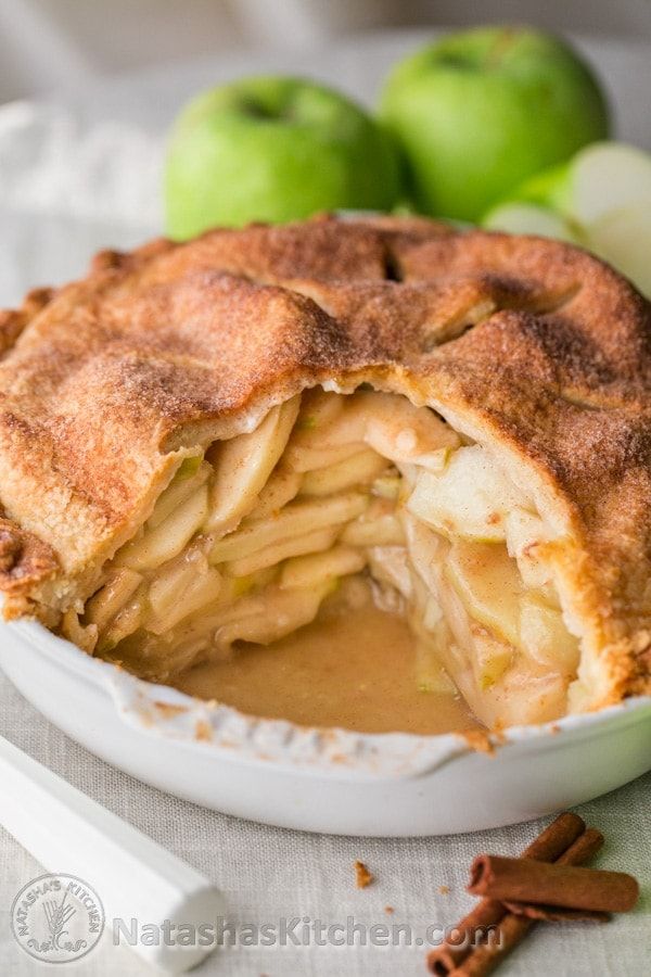 A slice removed from a deep-dish apple pie, revealing thick layers of baked apple slices and a pool of caramel-colored sauce.
