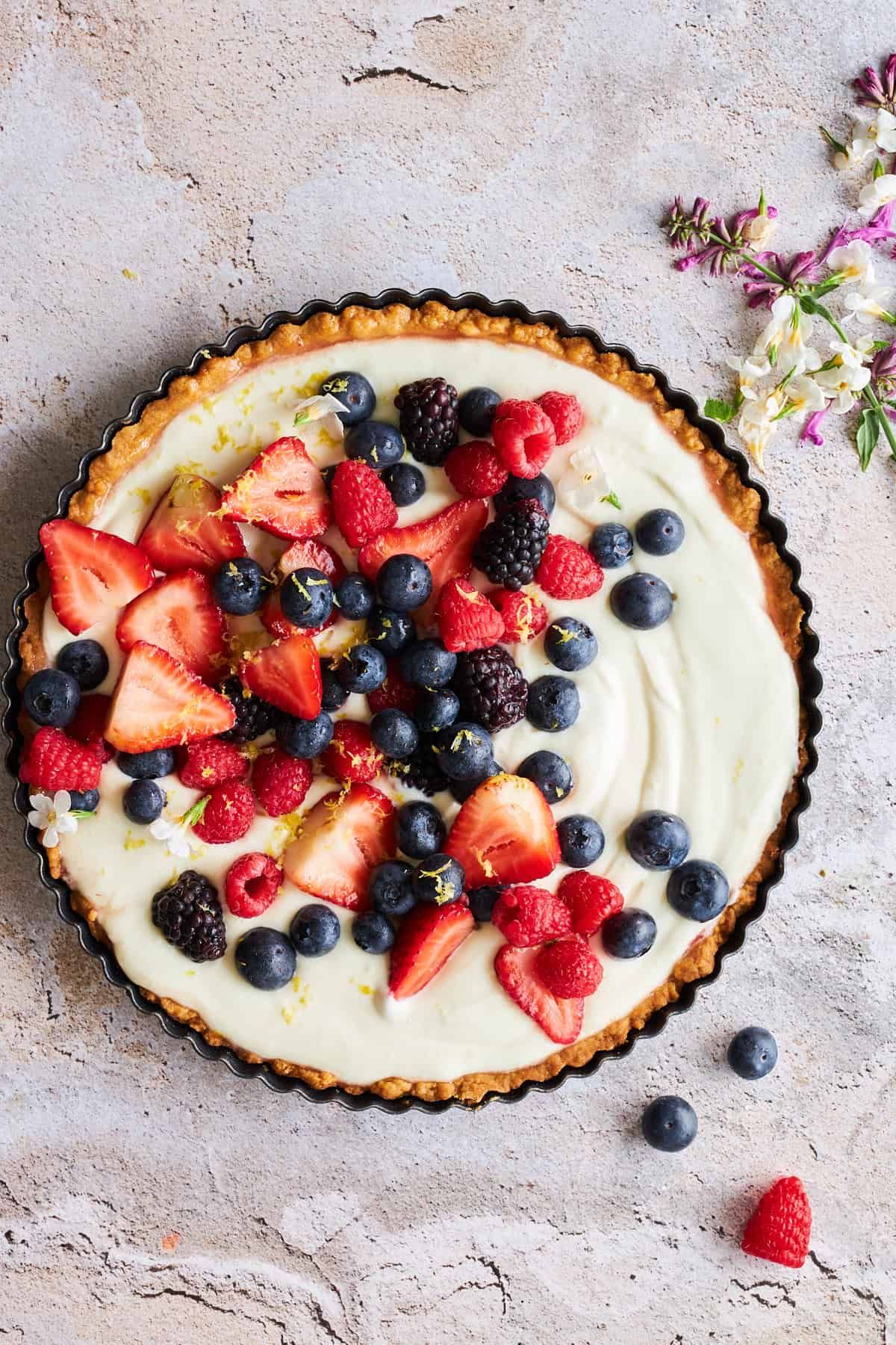 Round fruit tart with a crimped crust, creamy white filling, and fresh strawberries, blueberries, raspberries, and…