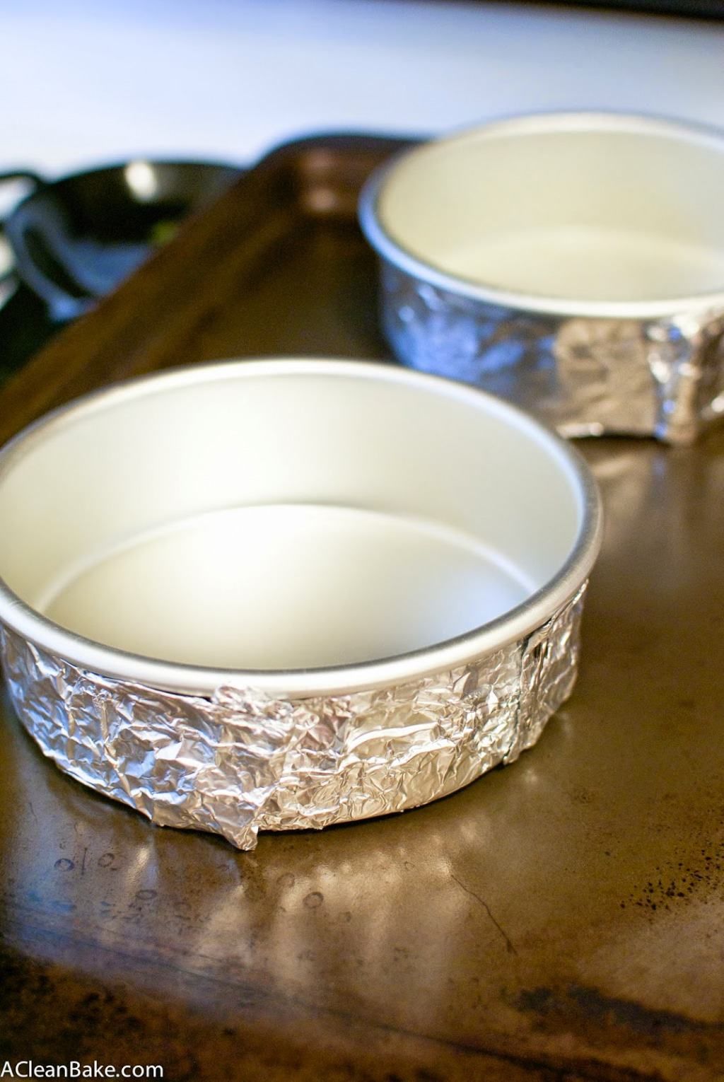 Two round aluminum baking pans, each with aluminum foil wrapped around the outside, sitting on a baking sheet.