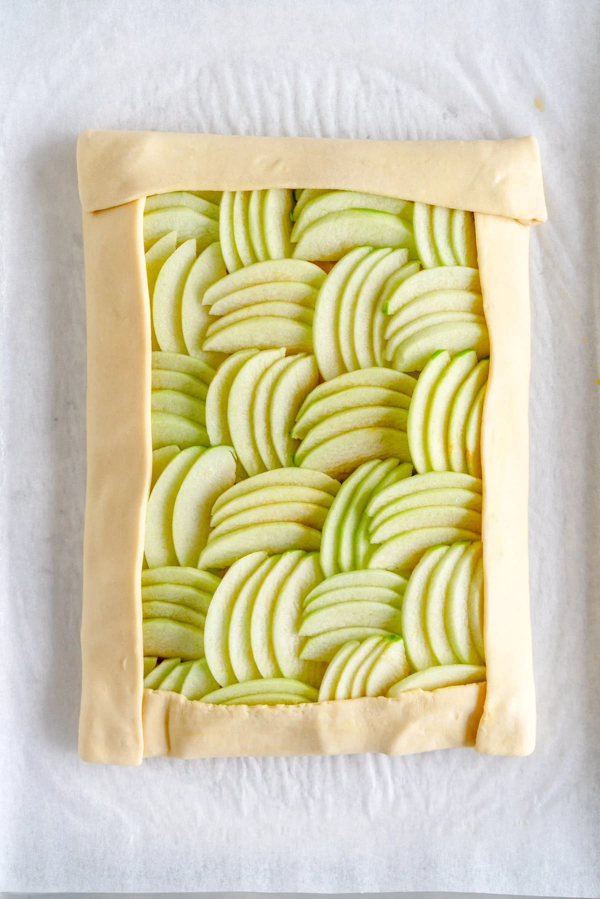 Unbaked apple galette with sliced apples arranged in pastry on parchment