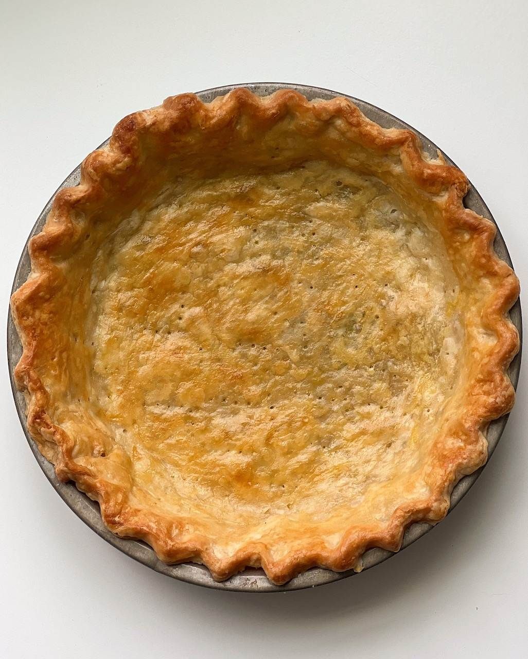 Baked golden brown pie crust in a metal pie plate with crimped edges.