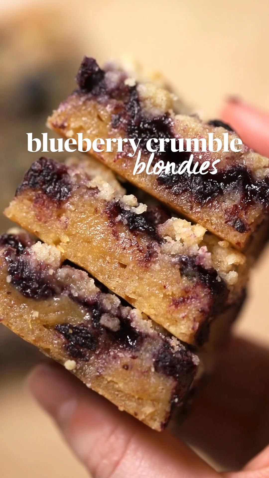 A stack of three blueberry crumble blondie bars, showing the fruit embedded in the bar and the crumbly topping.