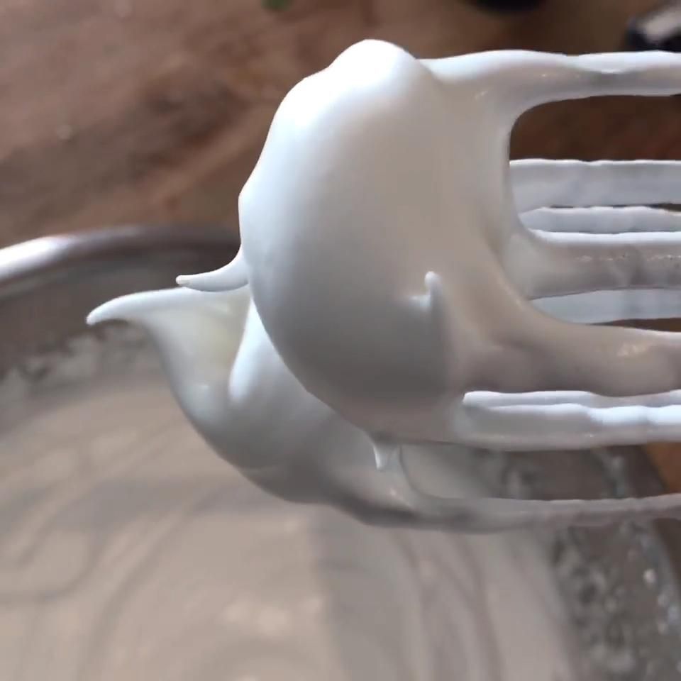 Close-up of a whisk with thick, white, whipped aquafaba forming stiff peaks