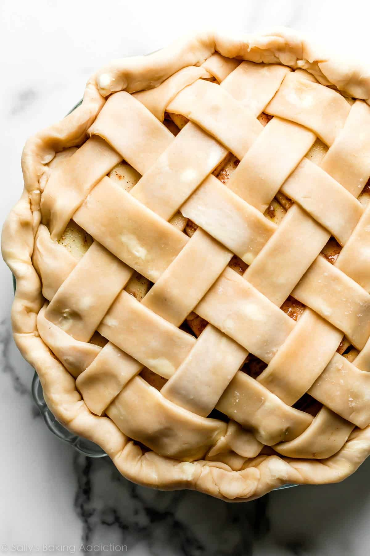 Close-up of an unbaked apple pie with a perfectly woven lattice crust and crimped edge in a glass pie dish.