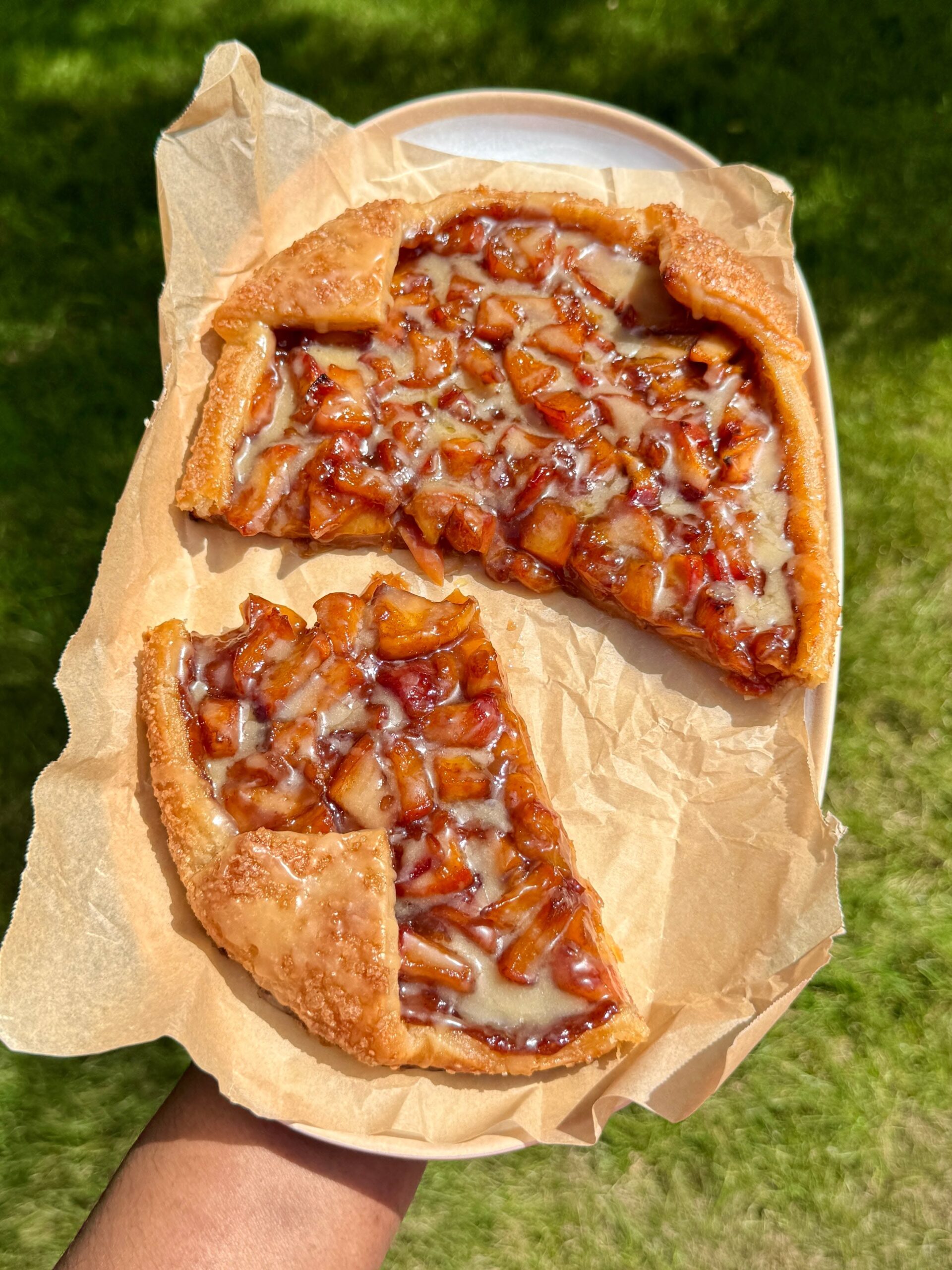 Fruit galette with a slice cut out, both drizzled with a light glaze, resting on parchment paper on a plate.