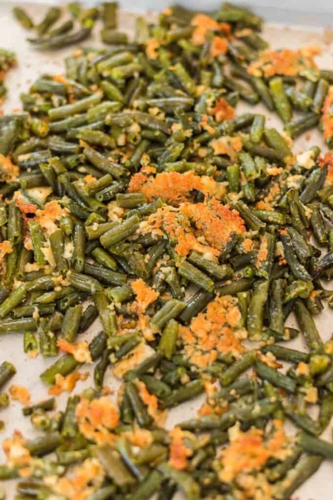 Baked green beans, some with crispy orange bits, spread on a light-colored baking sheet