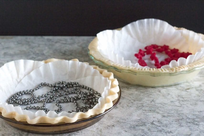 Two unbaked pie crusts in glass pie plates, lined with crumpled parchment paper and filled with pie weights.