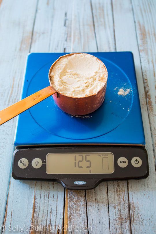 Measuring cup filled with flour on a digital kitchen scale showing 125 grams