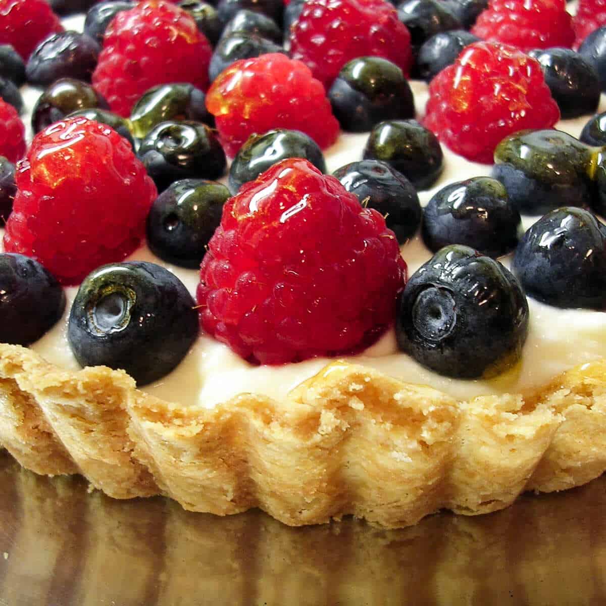 Fresh berry tart with blueberries and raspberries in a fluted crust on a silver platter.