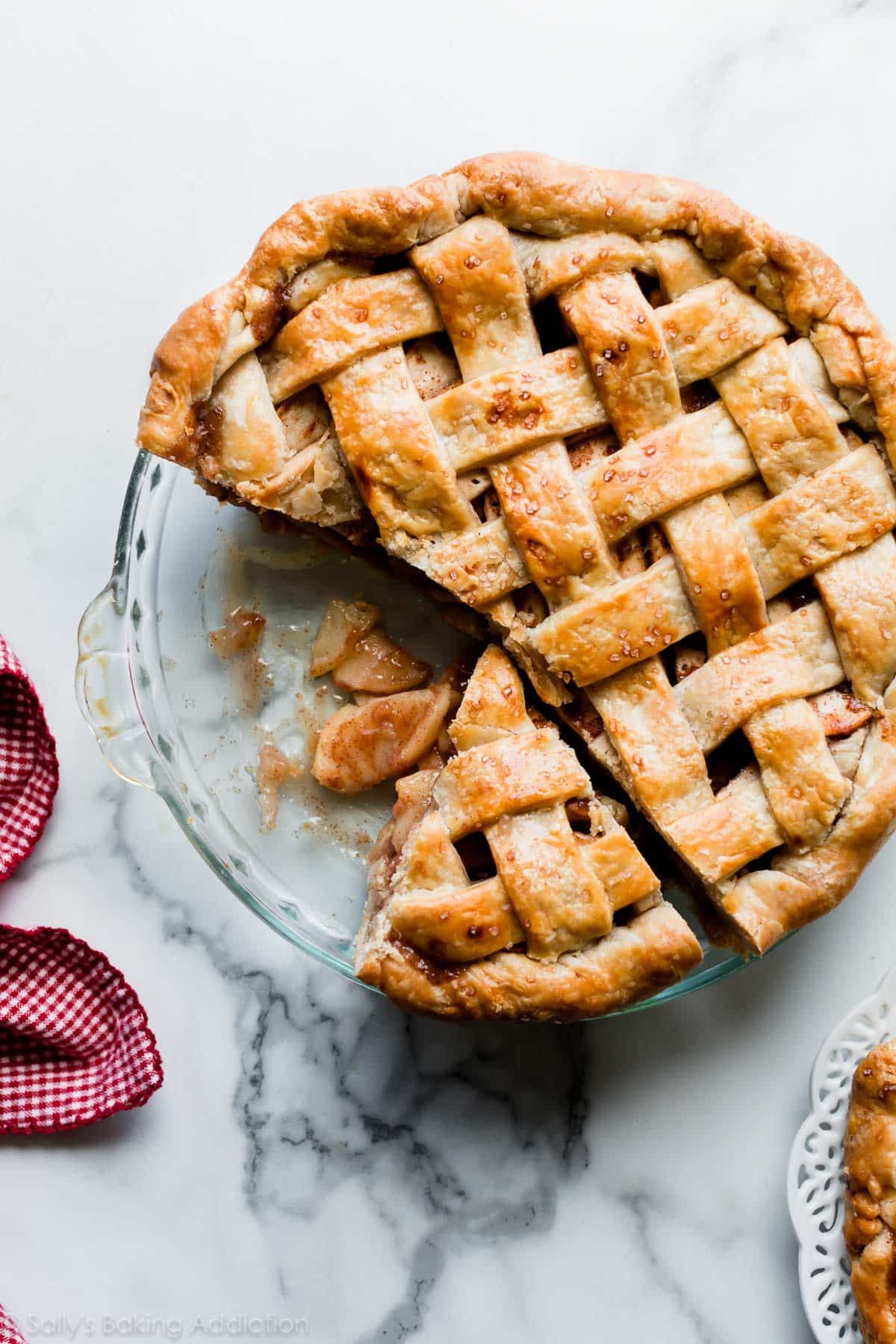 A whole baked apple pie in a glass dish with a lattice top, several slices removed