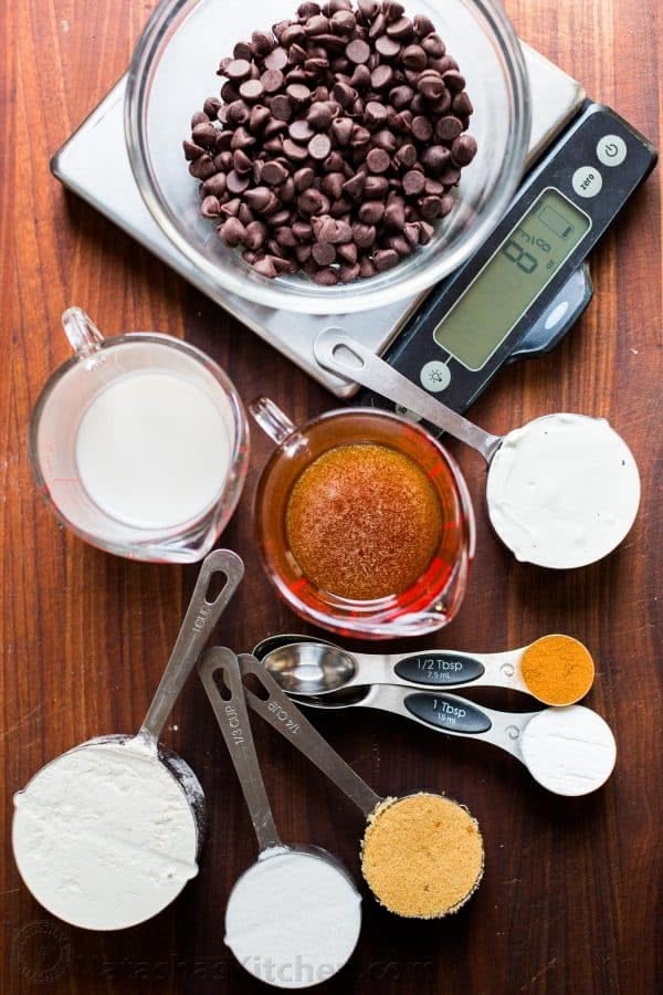 Overhead view of various baking ingredients measured with different tools: chocolate chips on a digital scale, milk in a…