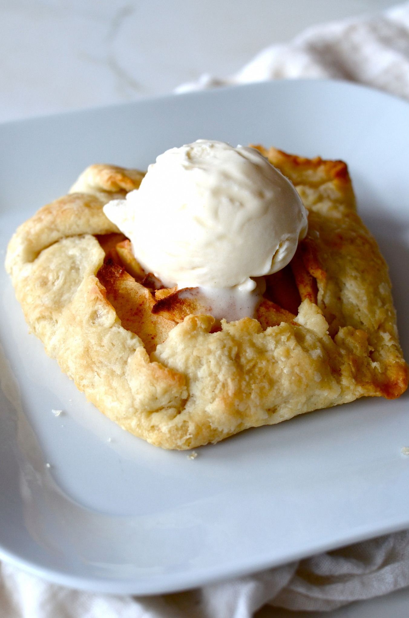 Square apple galette with a scoop of vanilla ice cream on a white plate