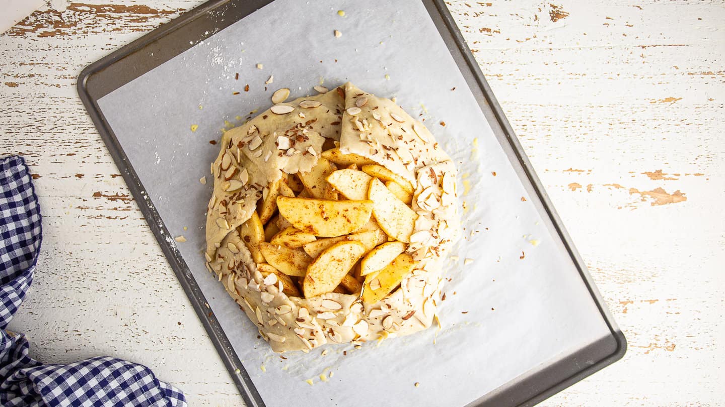 Unbaked apple galette on parchment with folded pastry edges