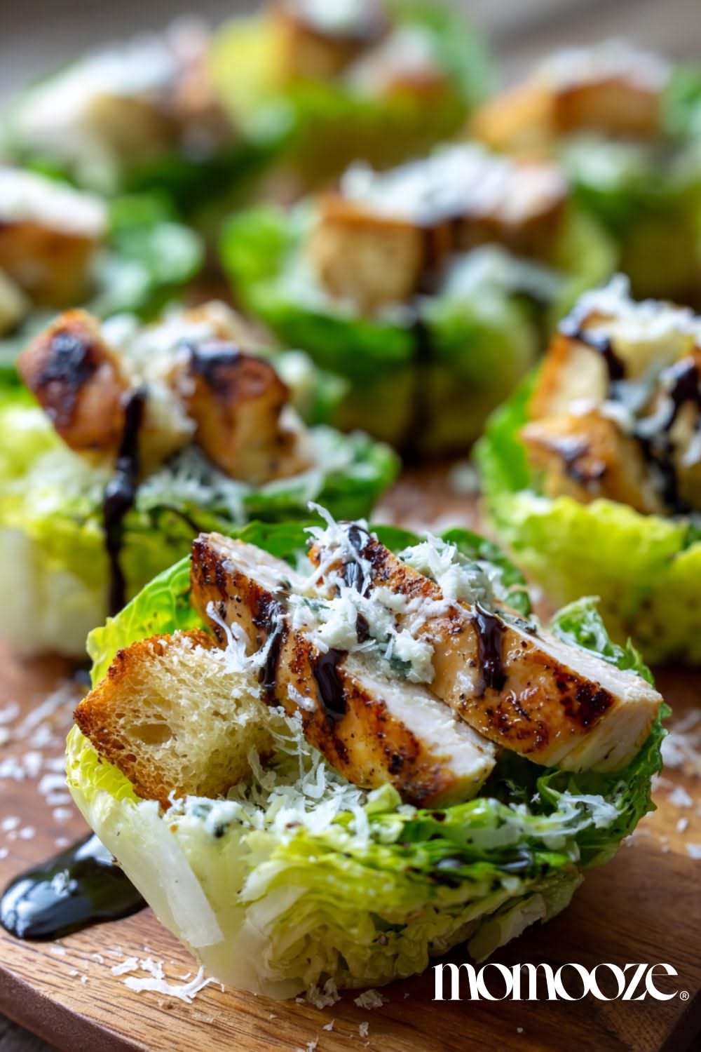 Close-up of several lettuce cups filled with grilled chicken, croutons, shredded cheese, and balsamic drizzle on a wooden…