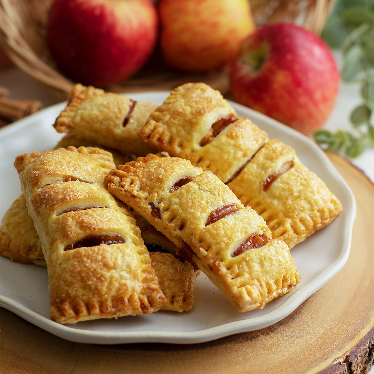 Apple turnovers on a white plate with whole apples in the background