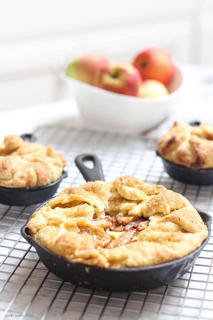 Three mini apple galettes with flaky crusts and apple filling, each baked in a small cast iron skillet on a cooling rack.