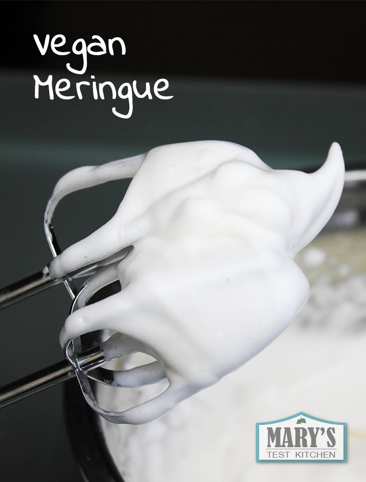 Close-up of an electric mixer beater coated in fluffy, white whipped aquafaba, showing stiff peaks.