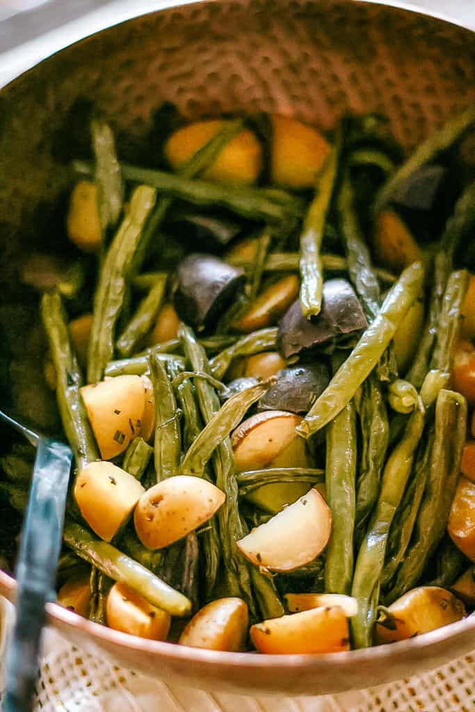 Roasted green beans with halved small potatoes in a copper bowl