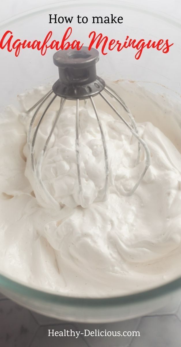 Close-up of fluffy white aquafaba meringue mixture with stiff peaks, with a whisk partly submerged in the bowl.