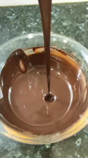 Melted dark chocolate pouring into a clear bowl, creating a small ripple