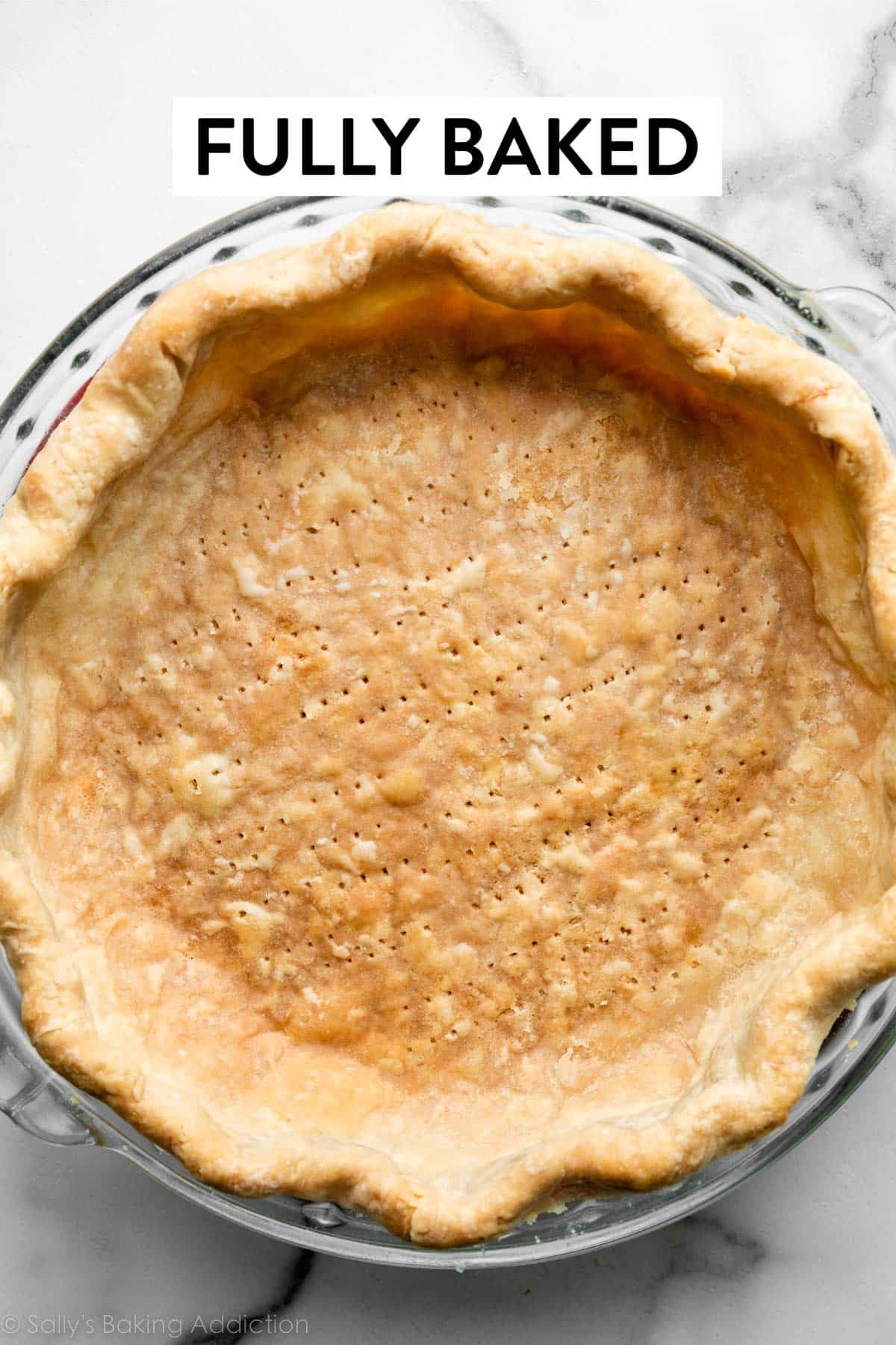 Close-up of a golden-brown, fully baked pie crust in a glass pie dish, pricked with many fork holes