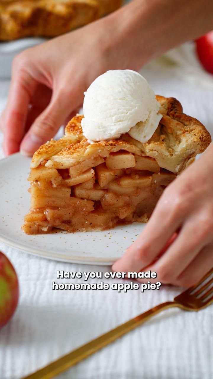 Hands serving a slice of apple pie topped with vanilla ice cream on a white plate.