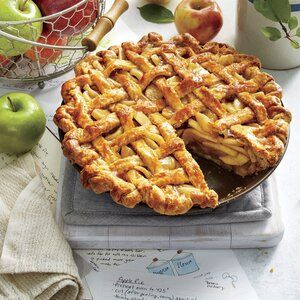 Baked apple pie with a golden brown lattice crust, a slice removed, surrounded by fresh apples.