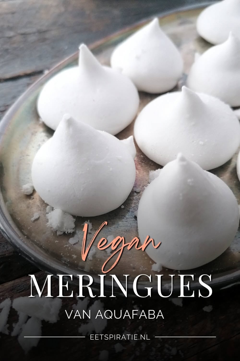 Several small, white, peaked aquafaba meringues resting on a metallic tray with some powdered sugar residue