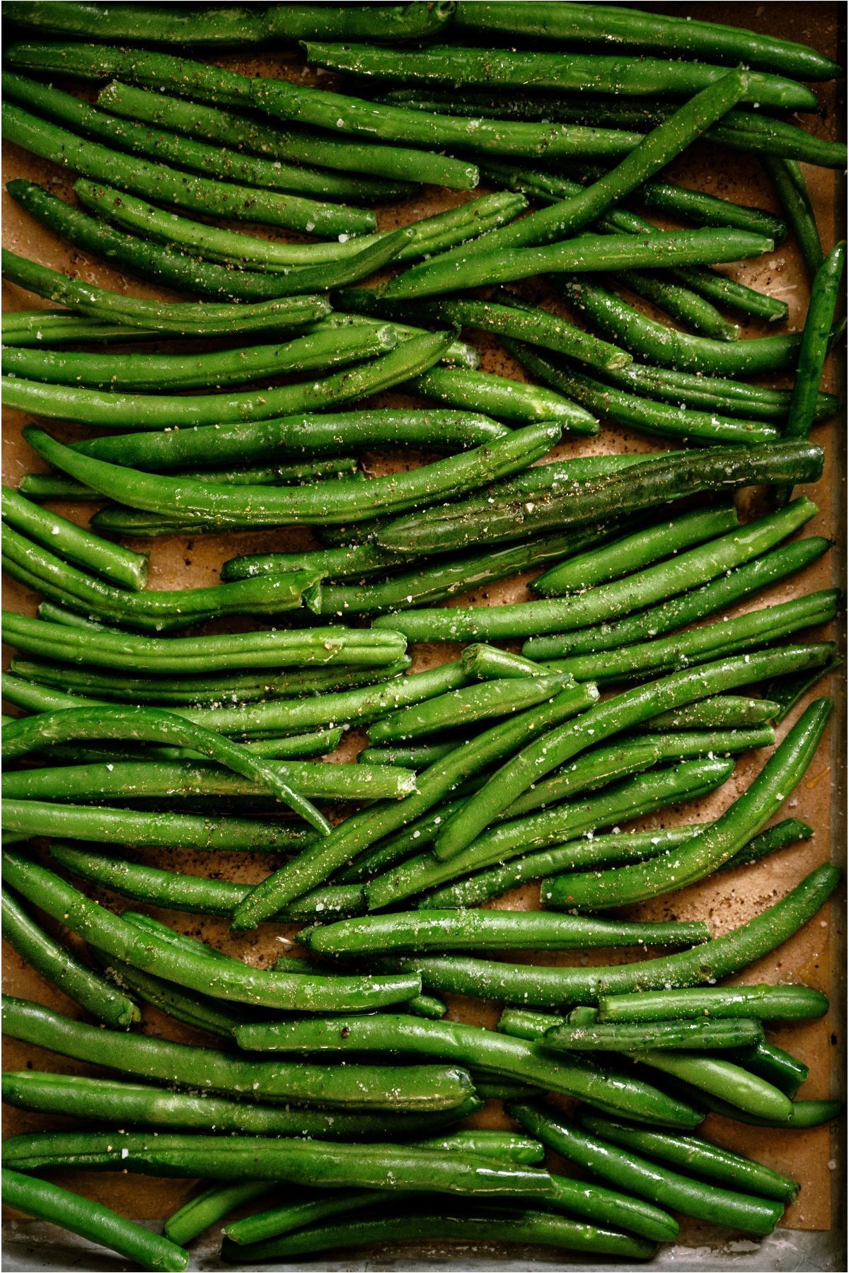Close-up of green beans seasoned with salt and pepper on a baking sheet