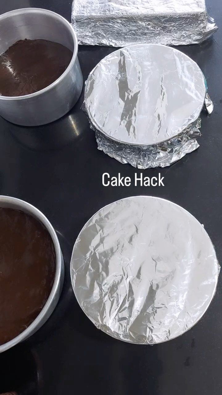Cake pans, one filled with batter, others wrapped in aluminum foil on a dark surface