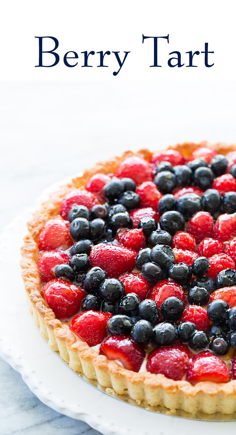 Close-up view of a baked tart filled with fresh strawberries, blueberries, and raspberries, on a white serving plate.