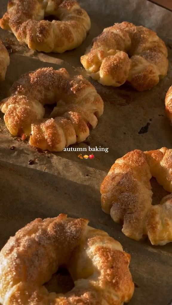 Close up of several crescent-shaped pastries covered in cinnamon sugar on a baking sheet.