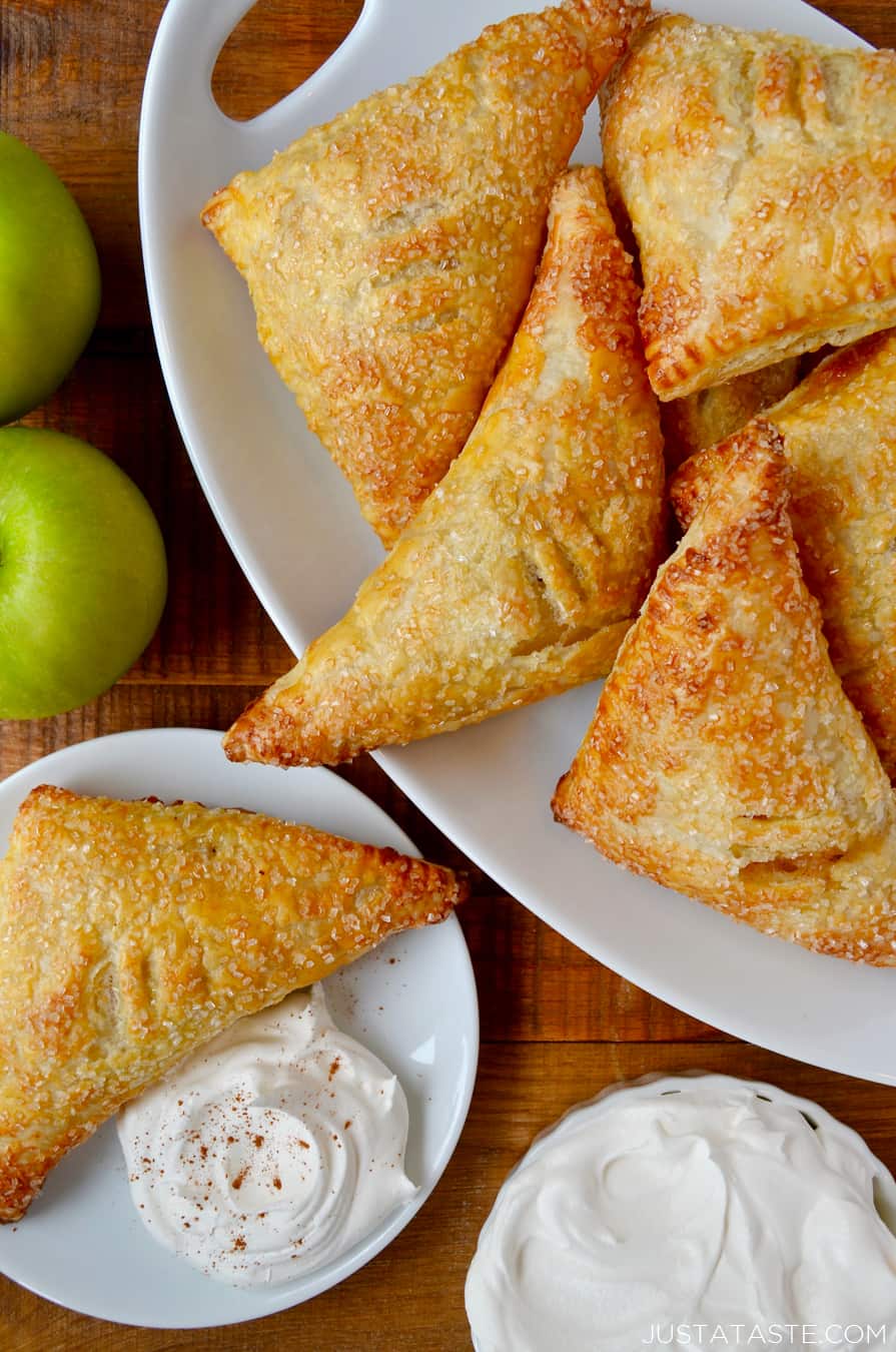 Golden apple turnovers on a white plate with a bowl of whipped cream